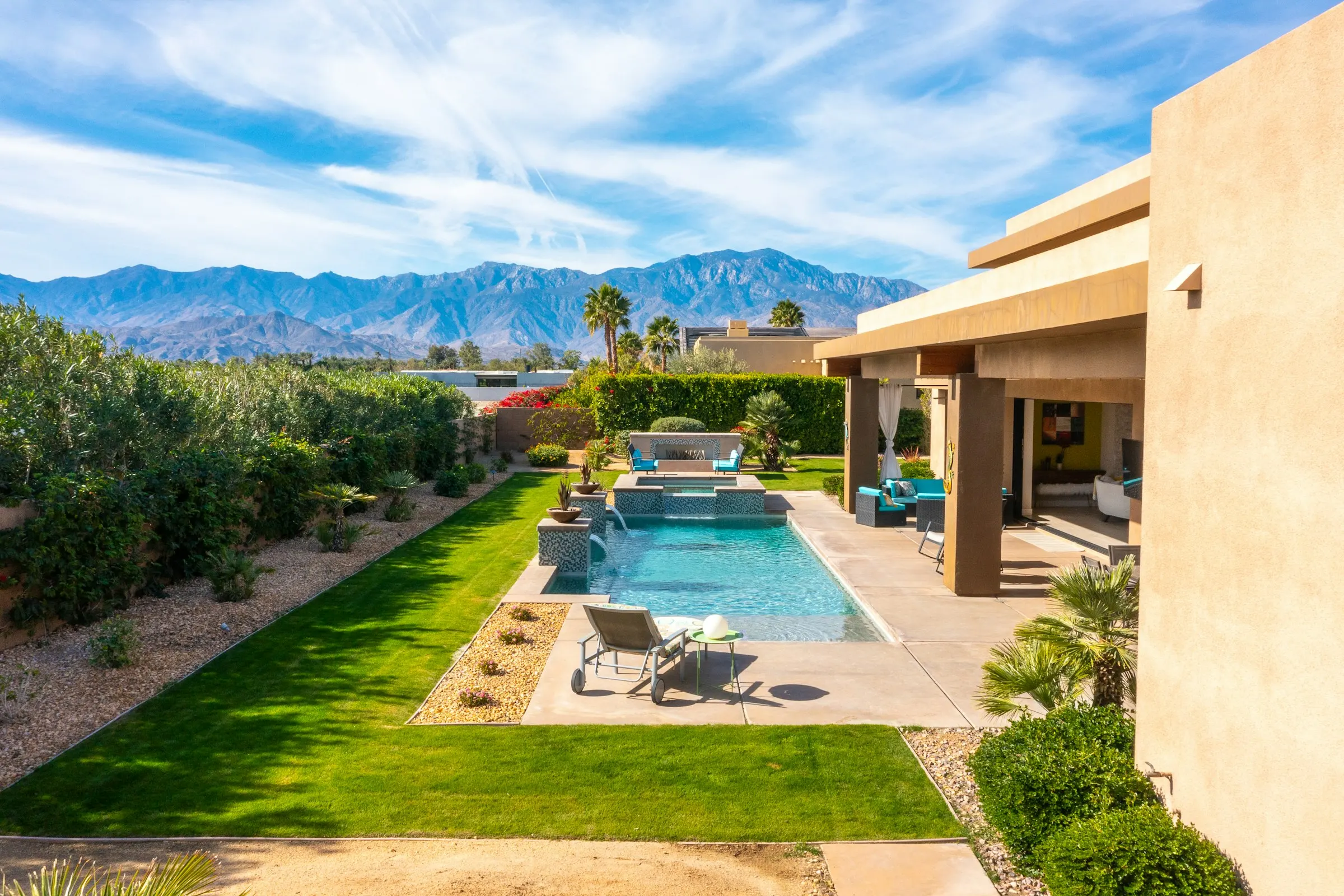 Backyard with a lawn strip, gravel beds, and a pool, with desert mountains beyond